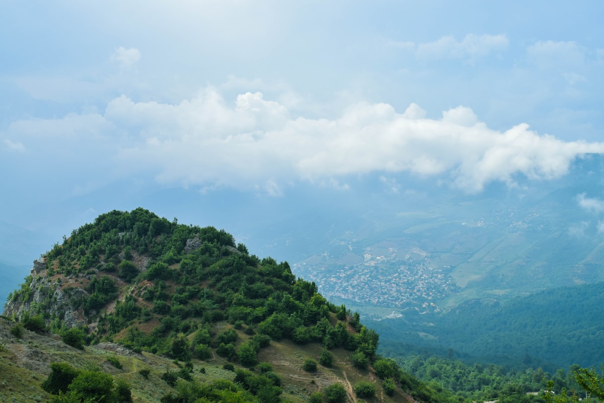 aerial photography of green field viewing mountain under white and blue sky during daytime