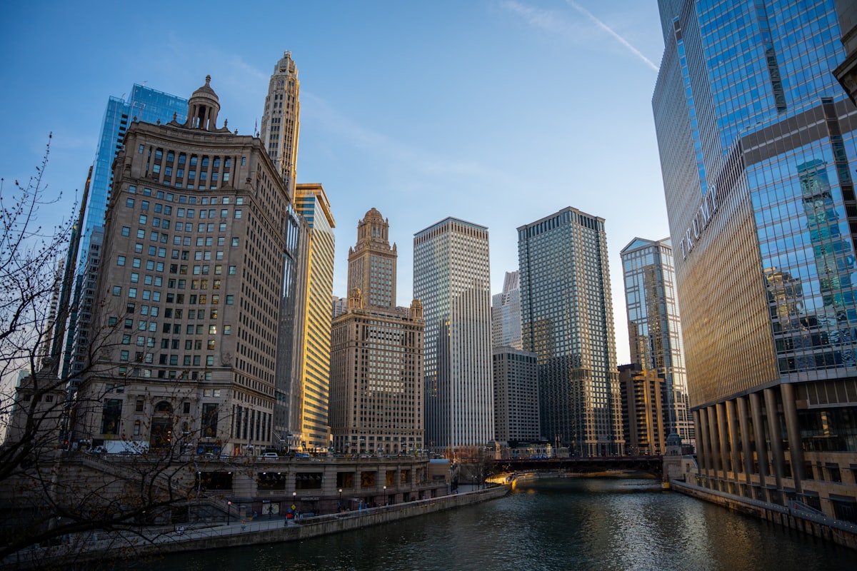 Modern skyscrapers line a river under a clear sky.