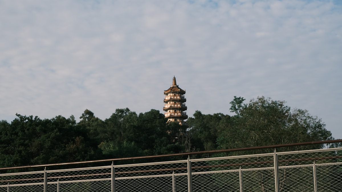 A pagoda rises above green trees under a cloudy sky.