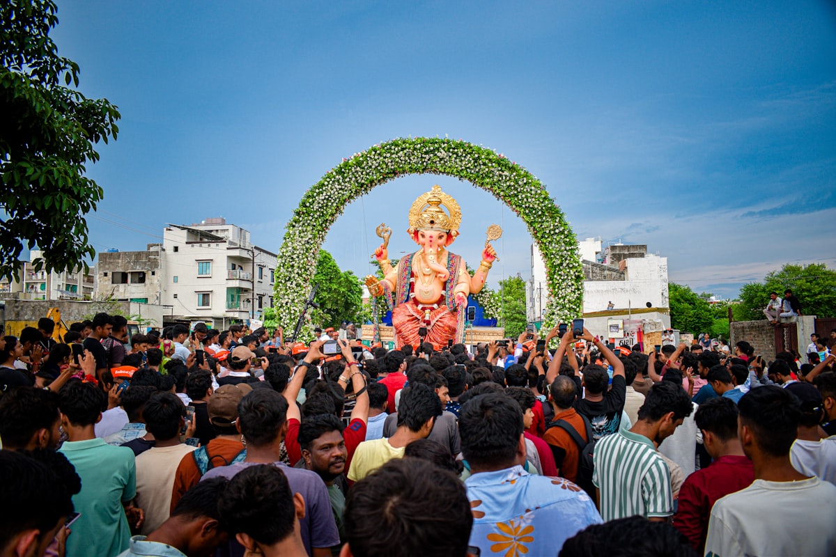 Crowd watches a large ganesha idol under an arch.