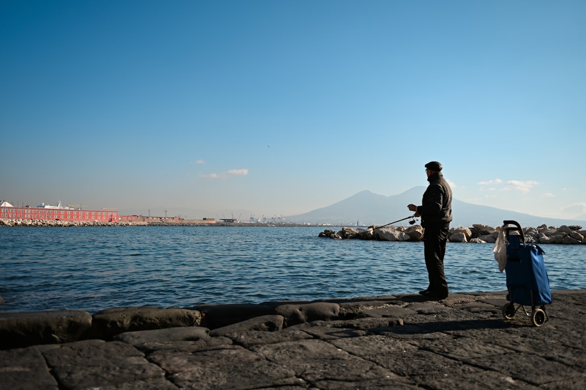 Man fishing by the sea with a mountain in background