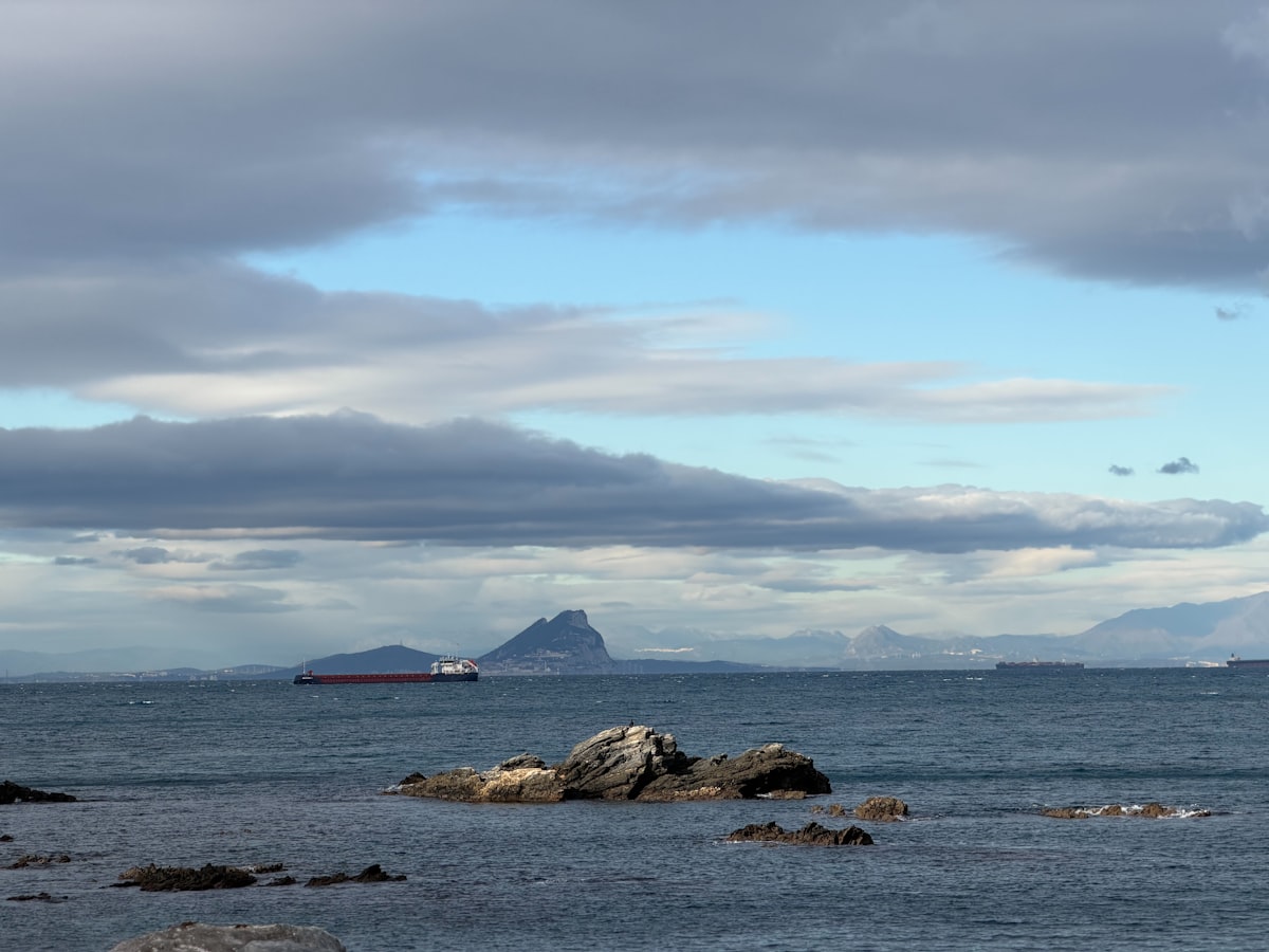 A cargo ship sails past a rocky outcrop at sea.