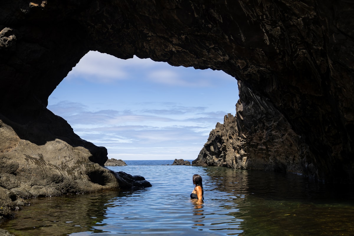 A person standing in a body of water under a cave