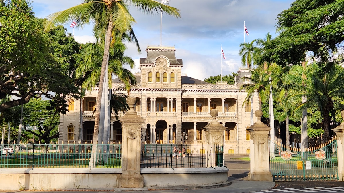 Iolani Palace with palm trees and a fence around it