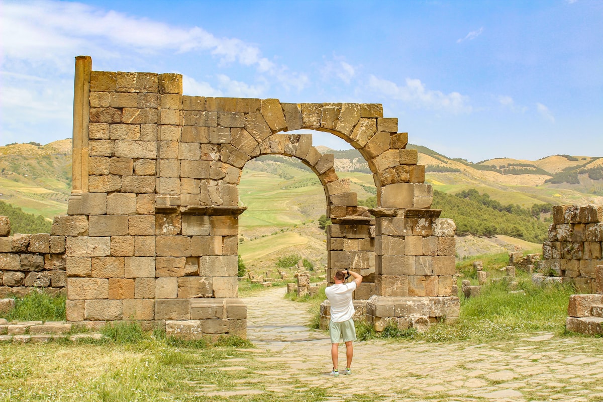 Man photographs ancient roman ruins and scenic landscape.