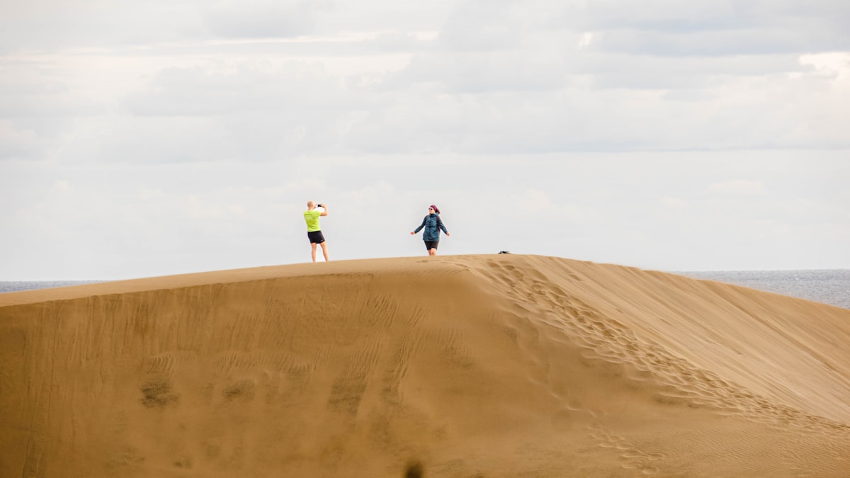 two people standing on top of a sand dune
