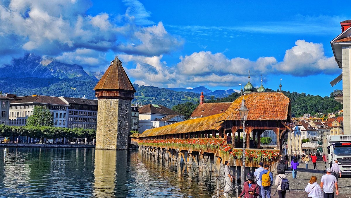 Covered wooden bridge over a river with mountains.