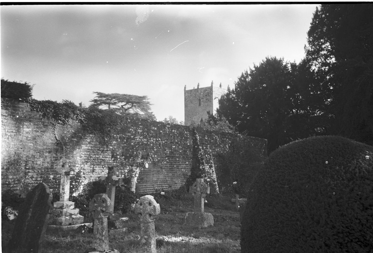 Old church tower behind a stone wall and graveyard.