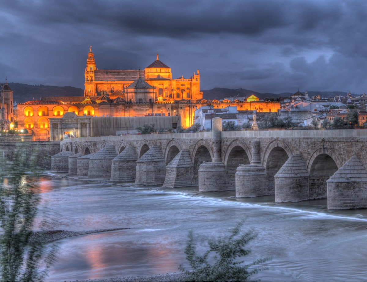 a bridge over a river leading to a large building with a large arched roof