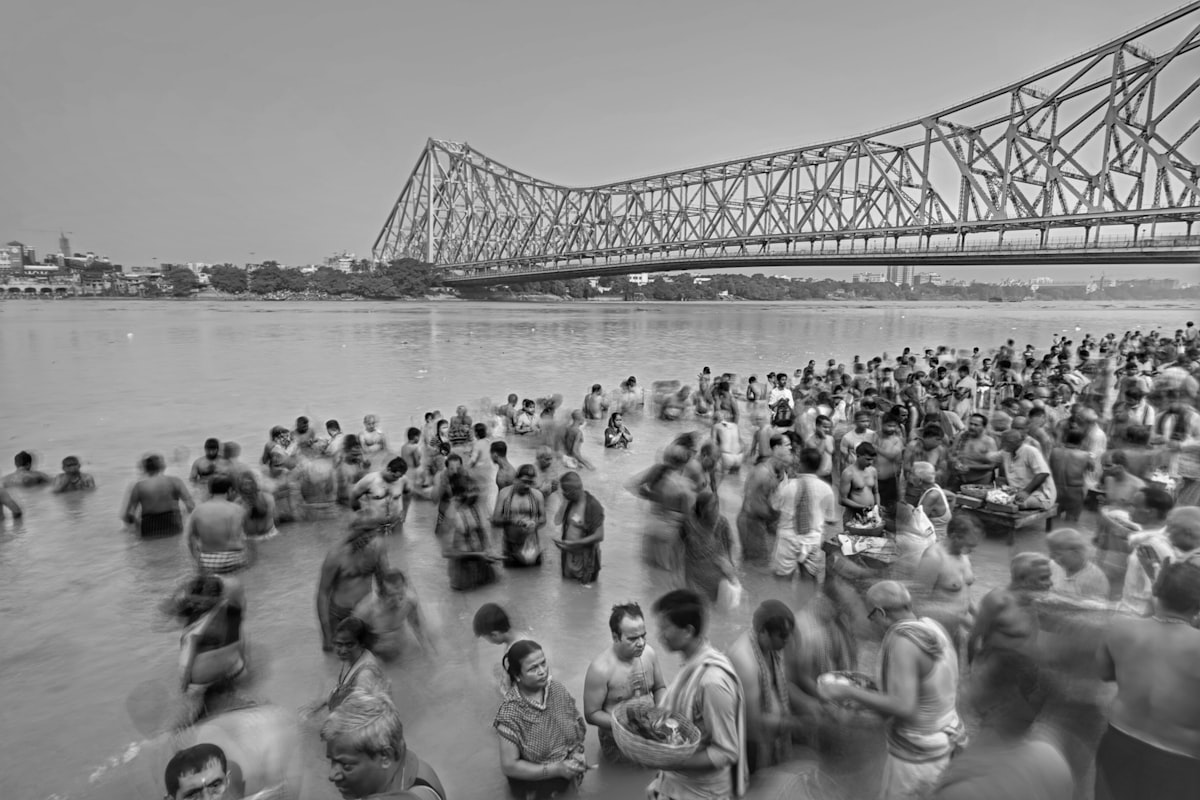 a large group of people standing in the water near a bridge