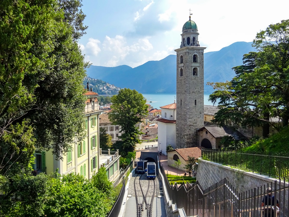 Trams ascend tracks past church tower towards lake.