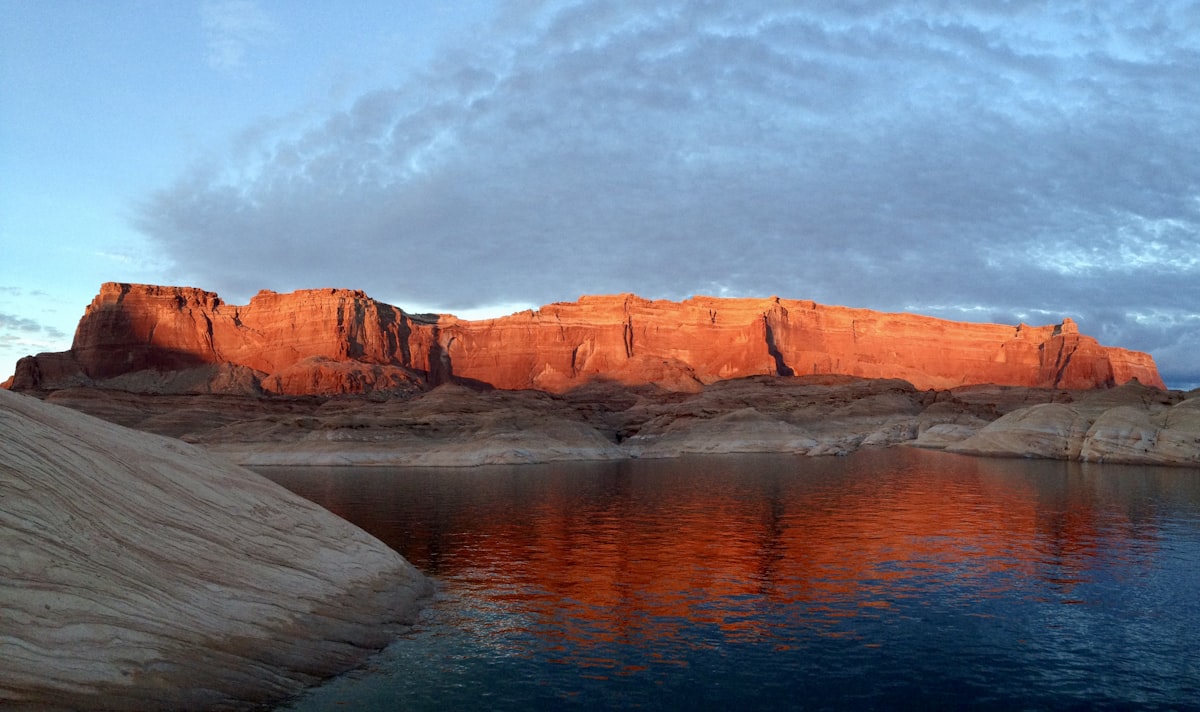 brown rocky mountain beside body of water under cloudy sky during daytime