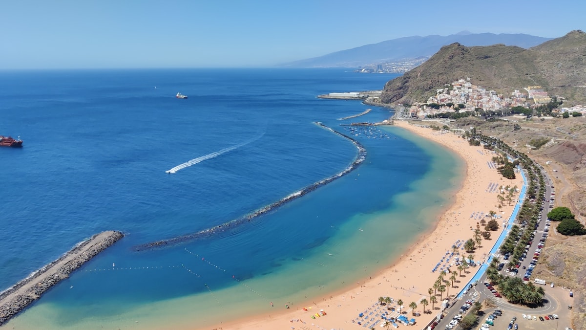 a beach with blue water and a sandy beach with a boat with Playa de Las Teresitas in the background