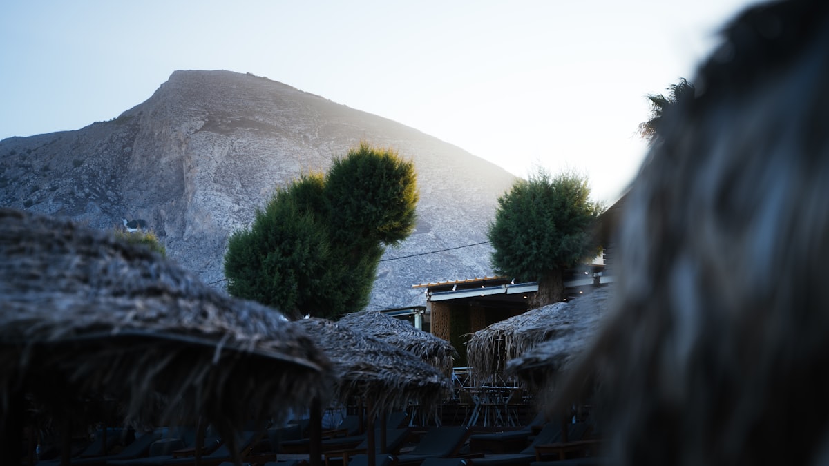 a group of straw umbrellas sitting in front of a mountain