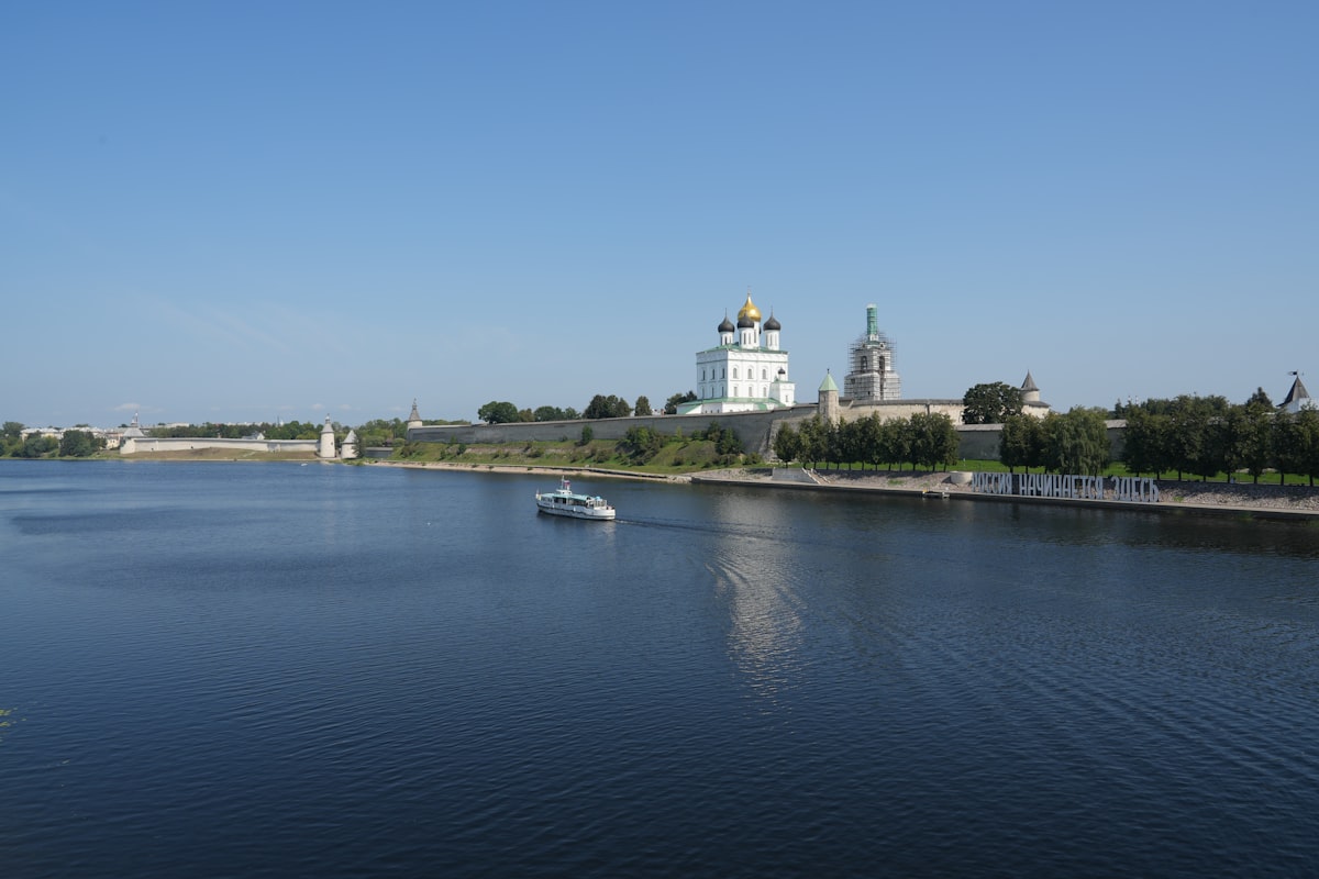 White boat sails on wide river near historic fortress.