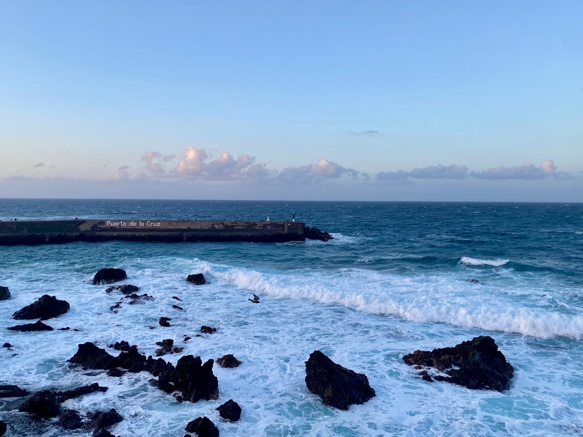 Rocky shoreline meets ocean waves under a blue sky.
