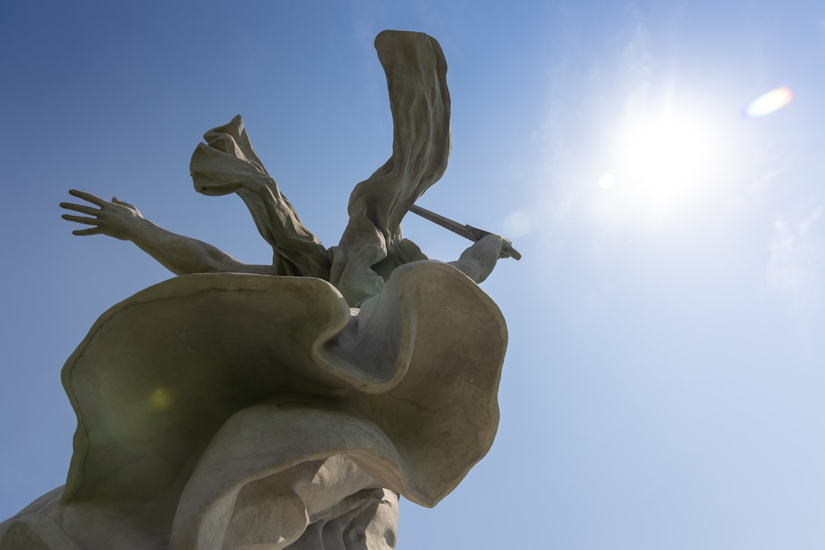 Statue against a bright blue sky with sun