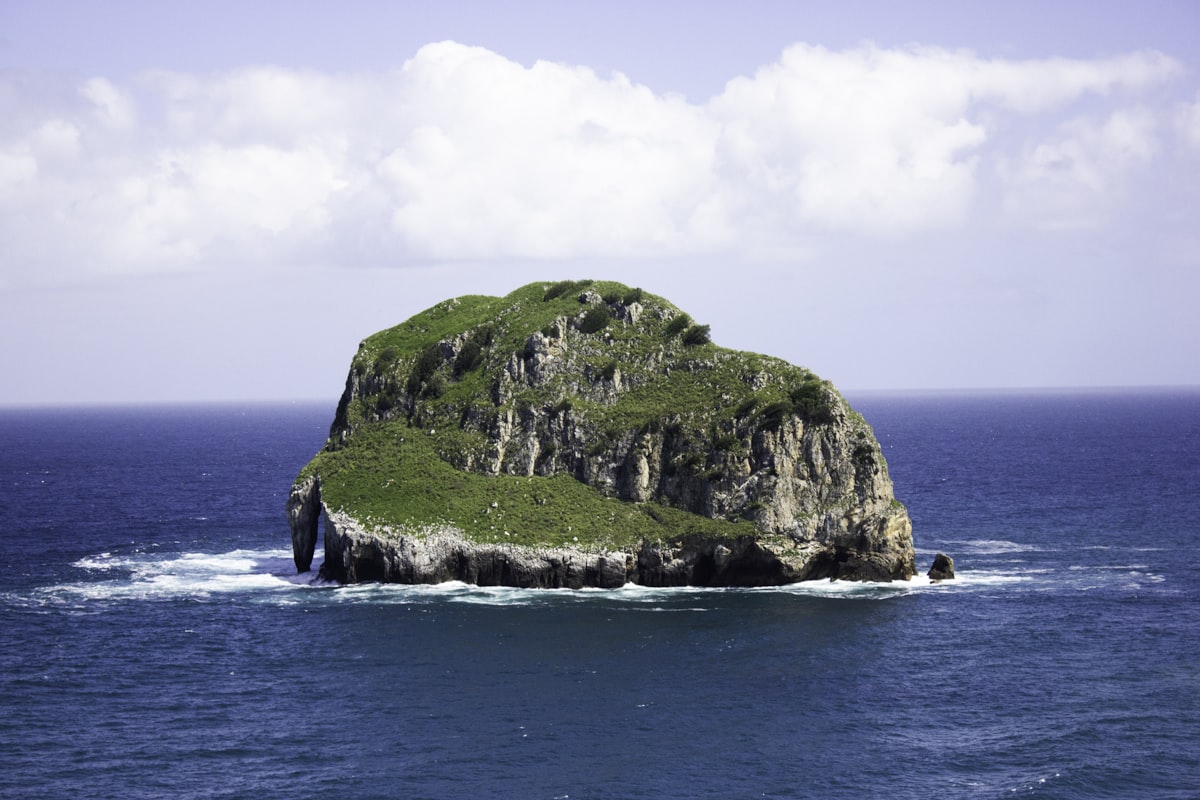 green and brown rock formation on sea under white clouds during daytime