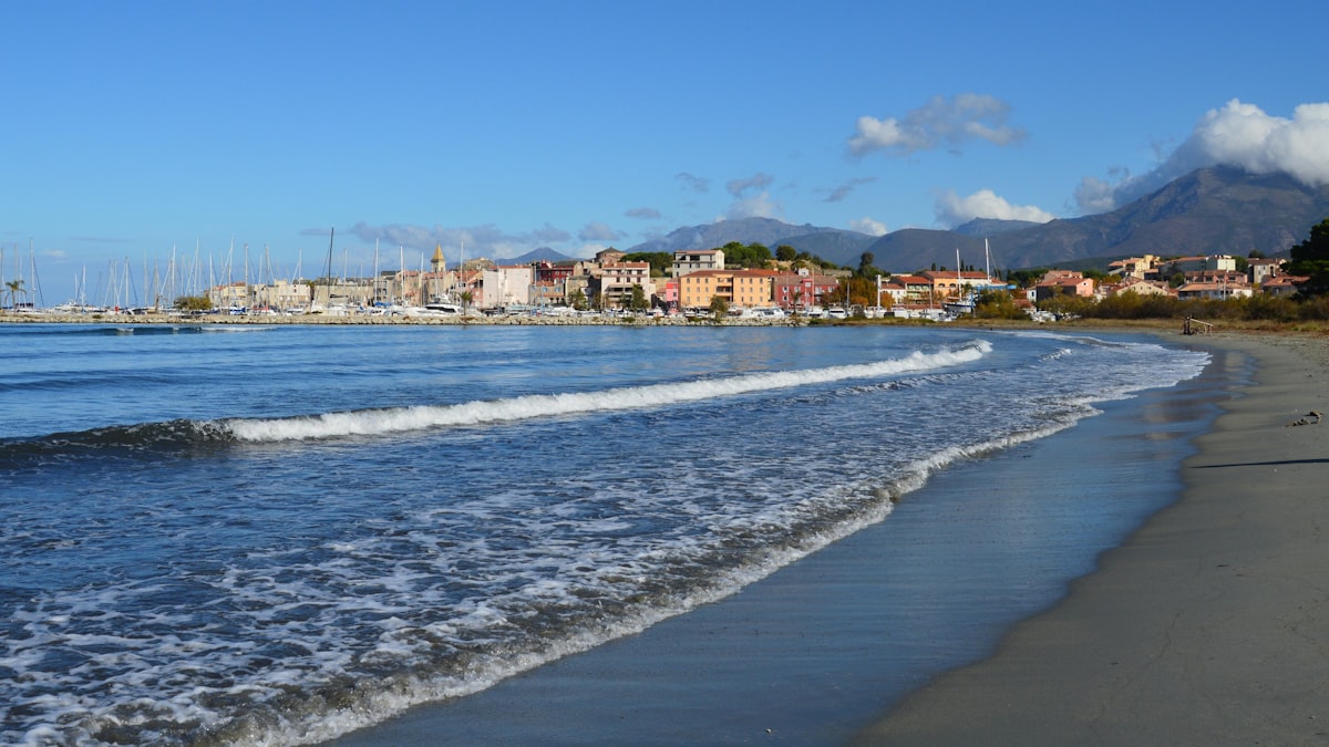 Waves gently lap a sandy beach with a coastal town.