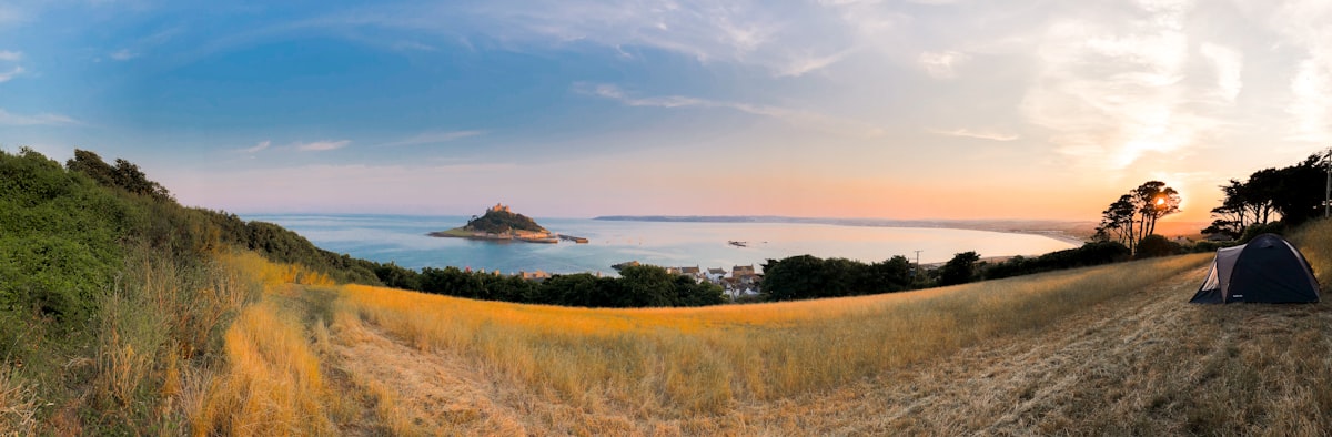 a field with a tent and a body of water in the distance