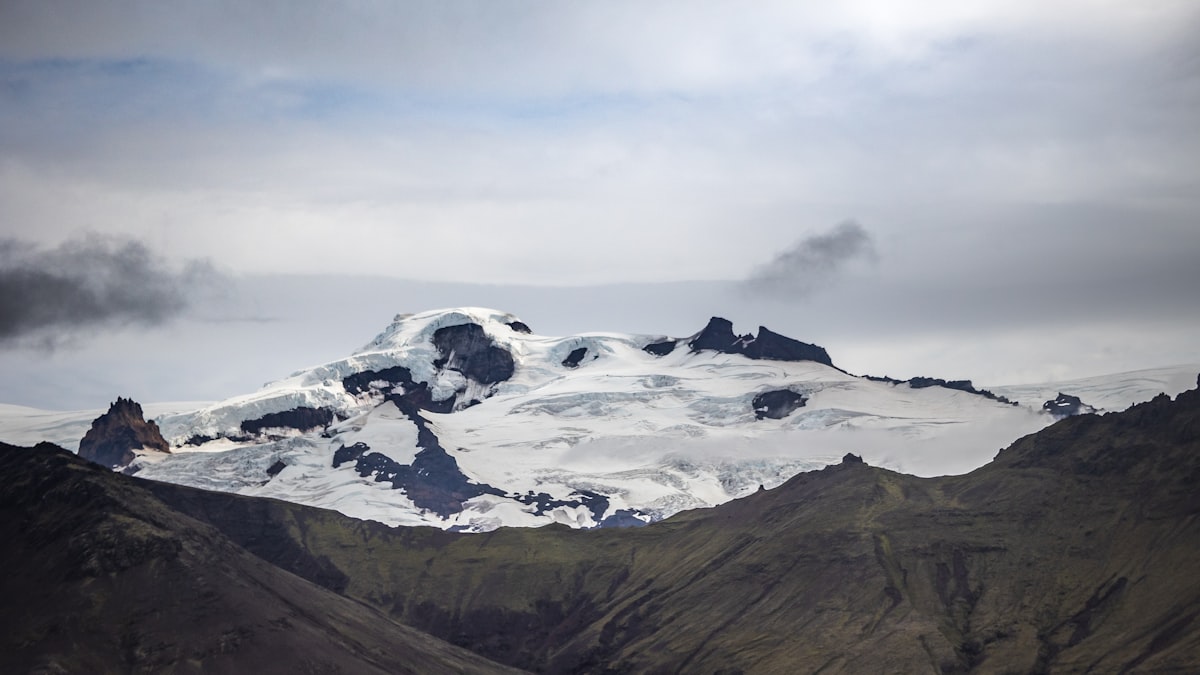 a mountain covered in snow with clouds in the sky