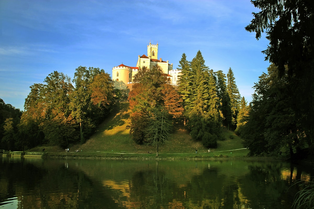 brown concrete building near green trees and lake under blue sky during daytime