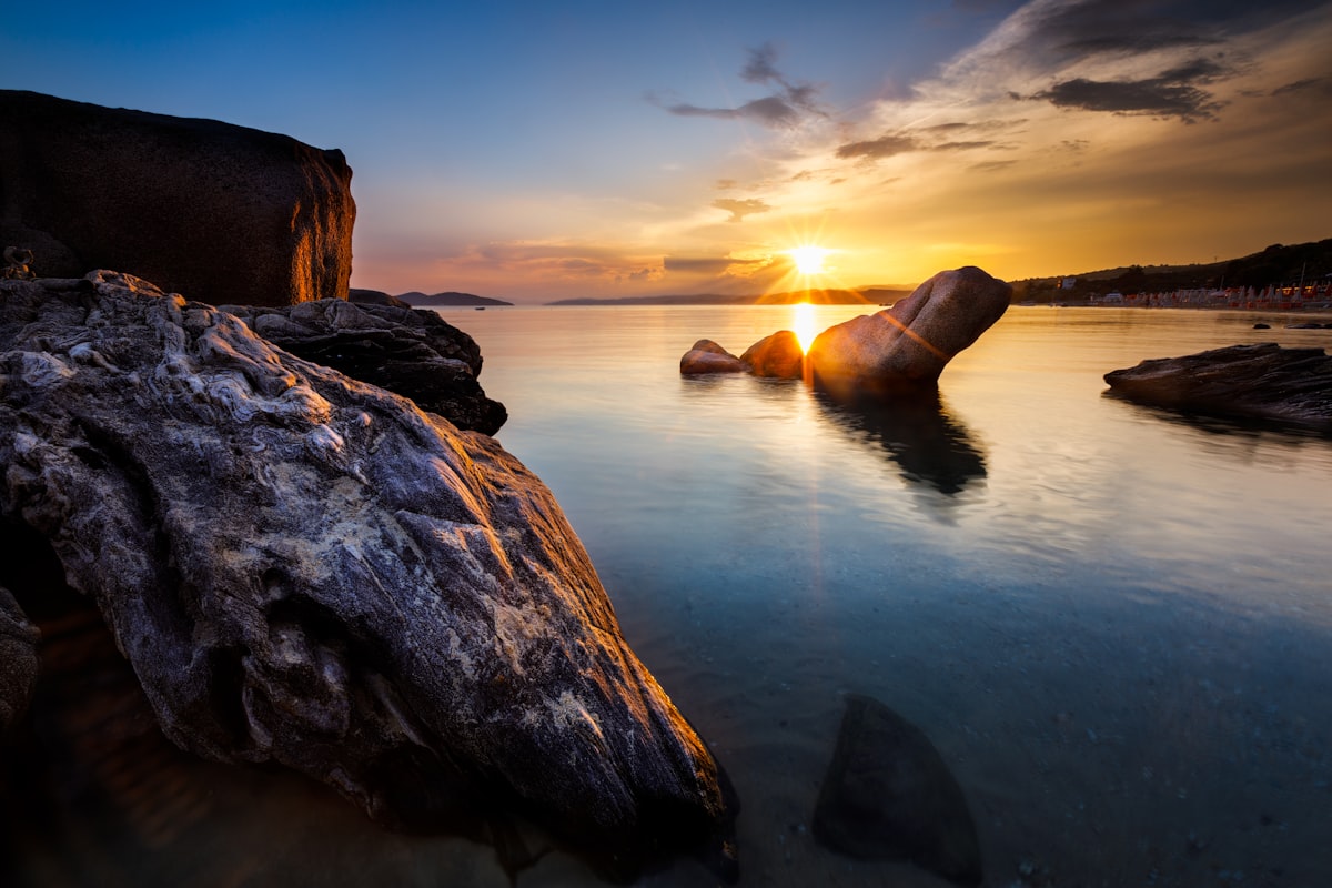 brown rock formation on body of water during sunset