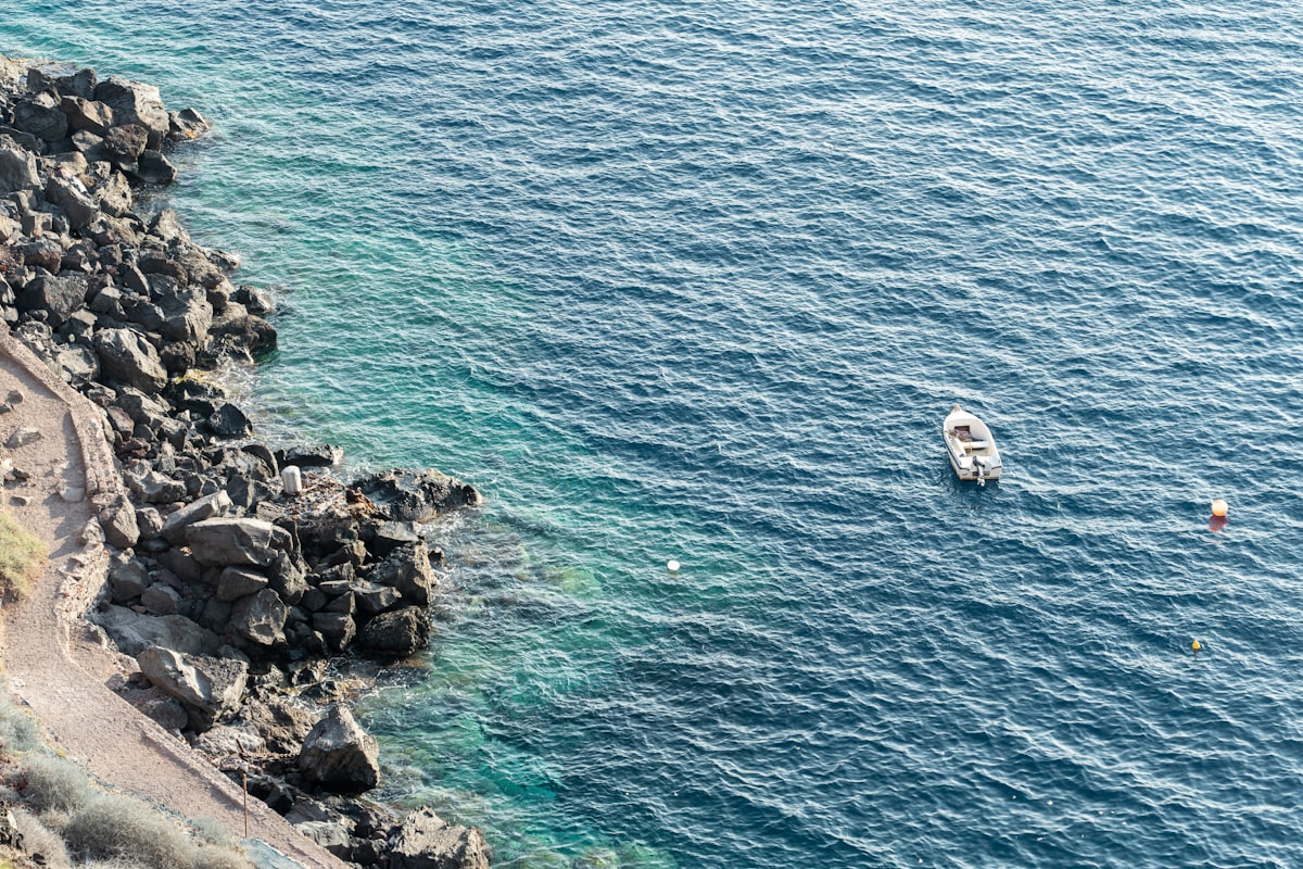 Boat floats in the blue sea near rocky coast.