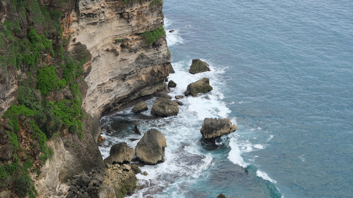 Rugged cliff face meets the ocean with crashing waves.
