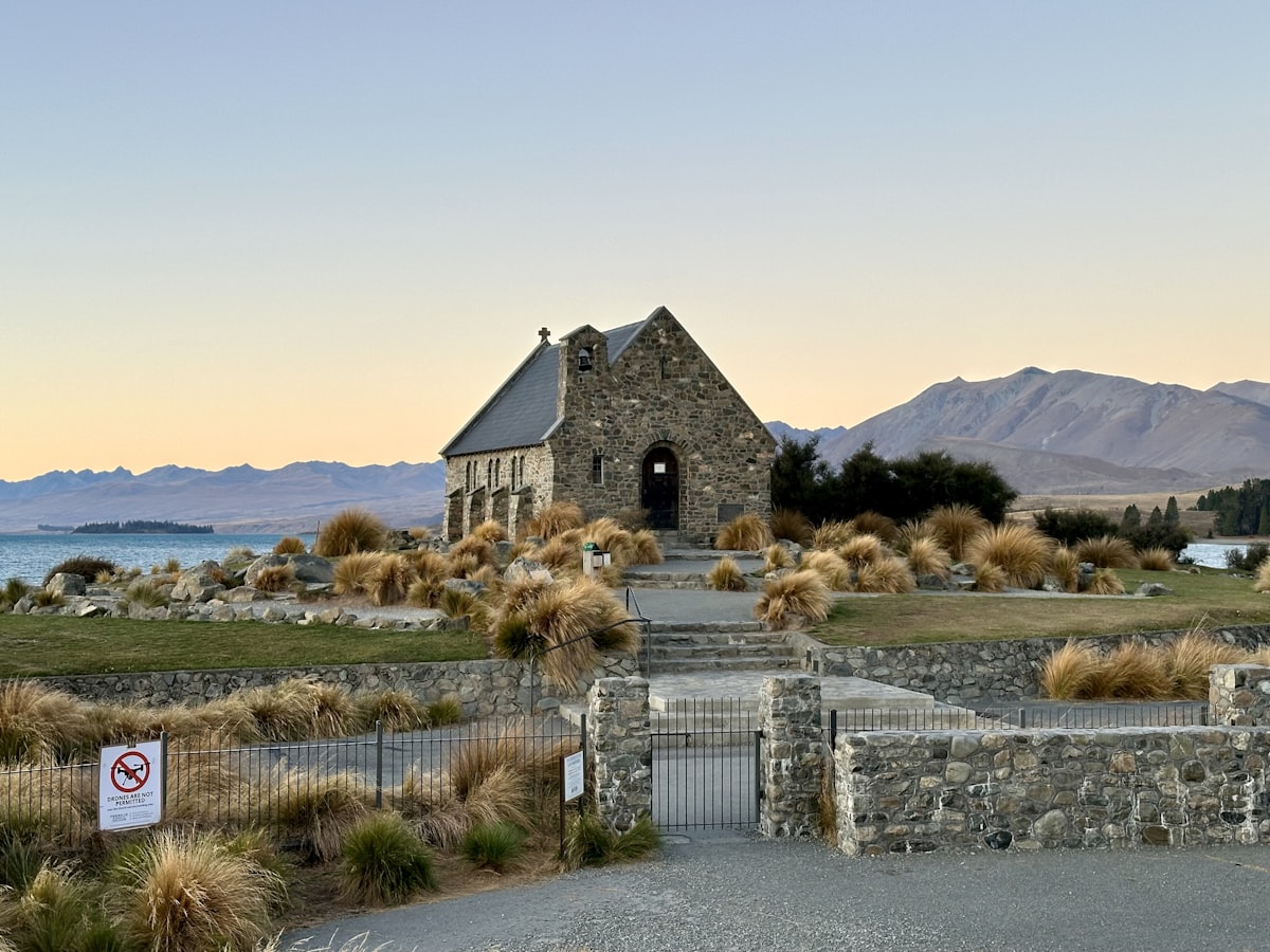 a stone church with a steeple surrounded by grass and mountains