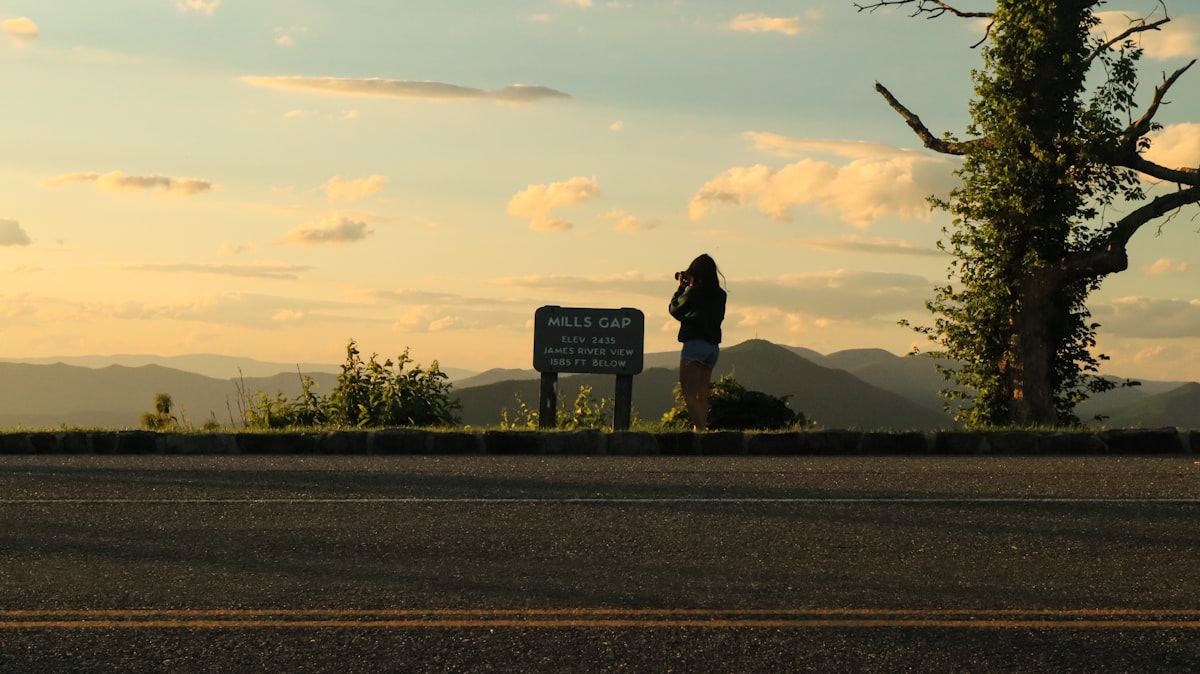 a woman standing next to a sign on the side of a road