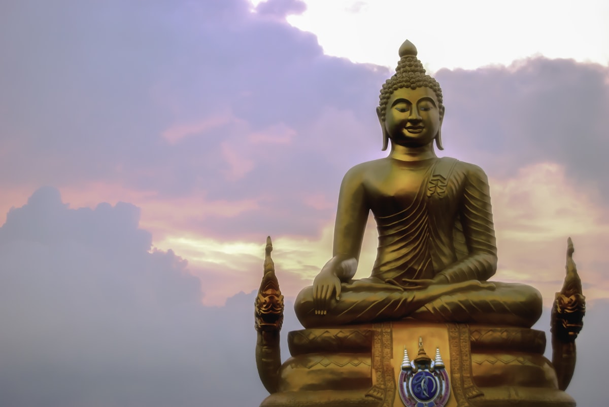 a golden buddha statue sitting in front of a cloudy sky