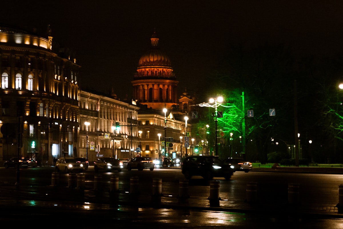 City street at night with illuminated buildings and cars.