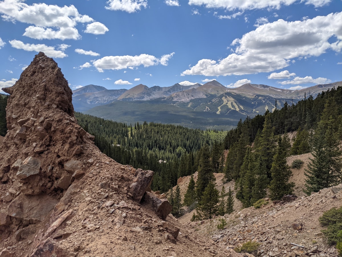 Rocky foreground with a lush mountain valley and distant peaks.