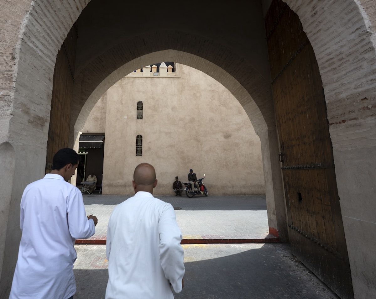 Two men walk through an archway into a courtyard.