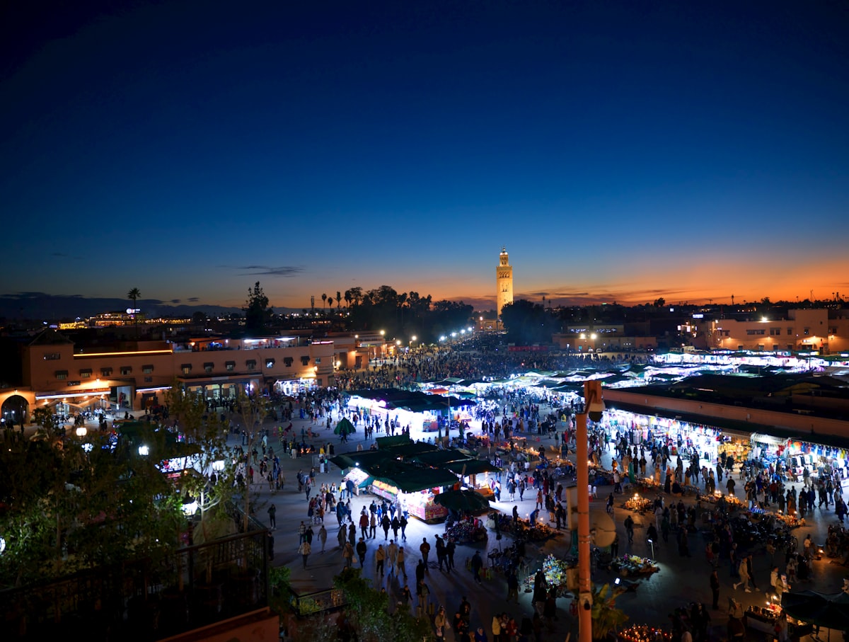 Busy marketplace at dusk with illuminated stalls and buildings.