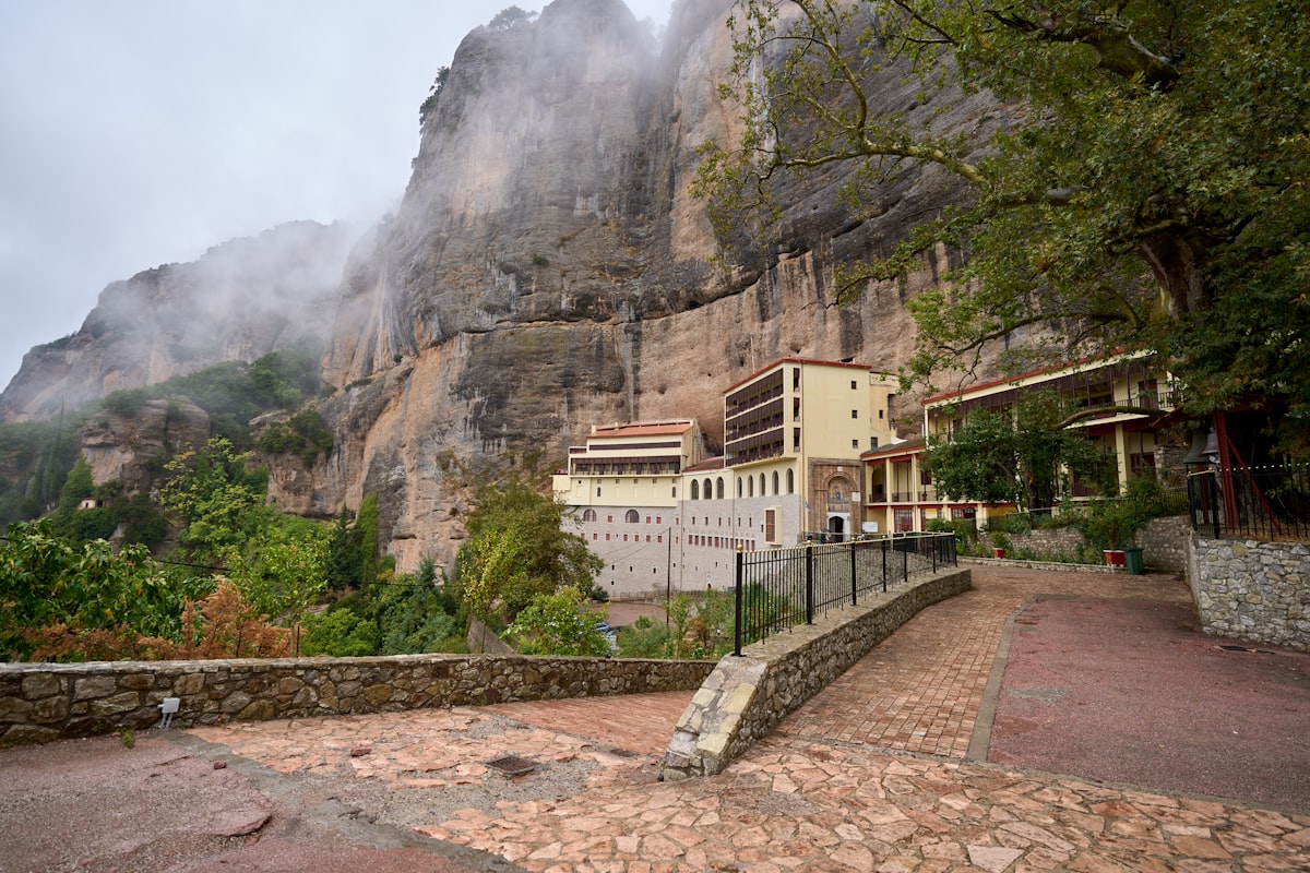 Monastery built into a steep, rocky mountainside with fog.