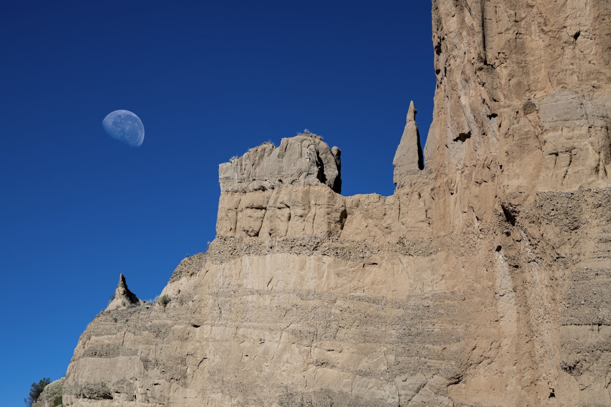 Rocky formations under a clear blue sky with moon.