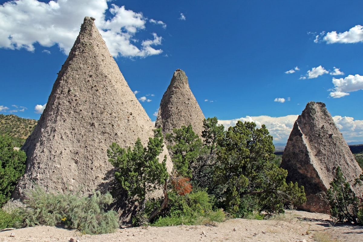 Cone-shaped rock formations with green bushes under blue sky