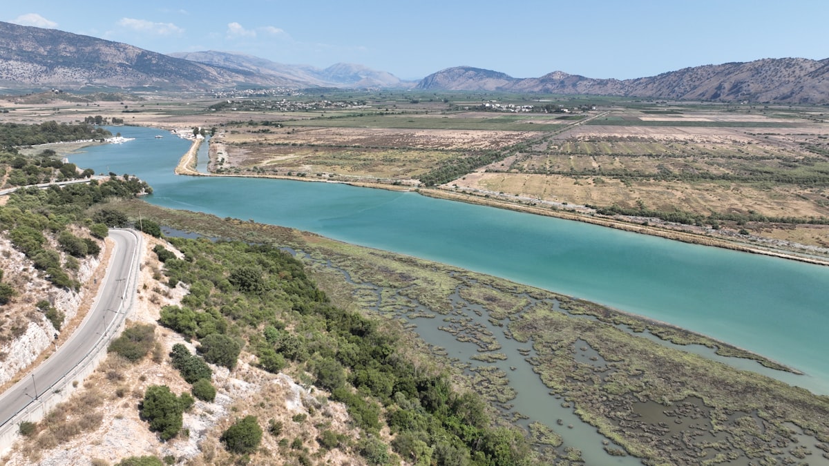 A wide river flows through a rural landscape with mountains.