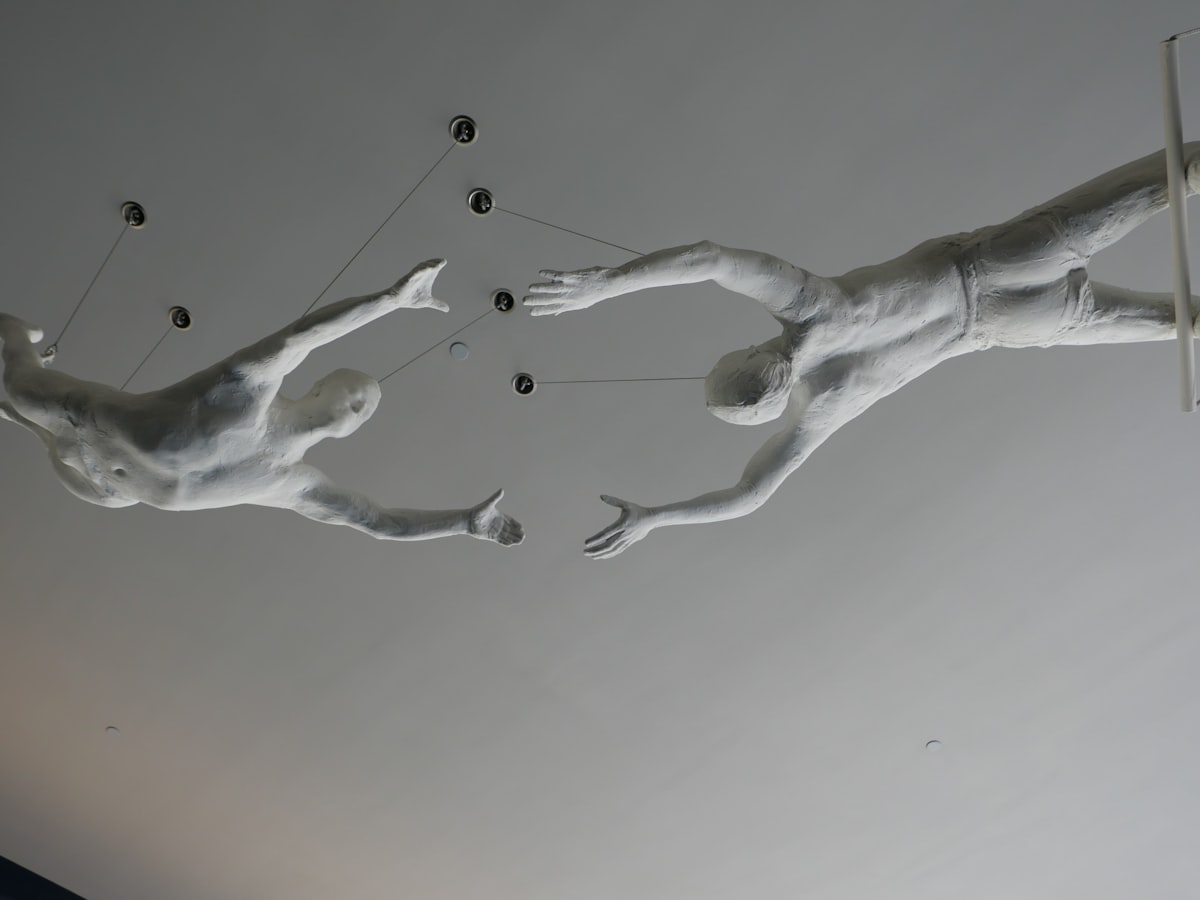 Two white sculptures of people reaching for each other