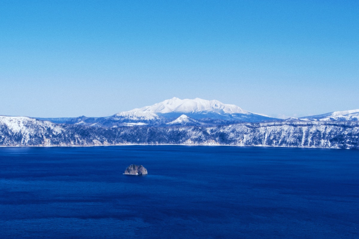 Snow-capped mountains rise above a deep blue lake.