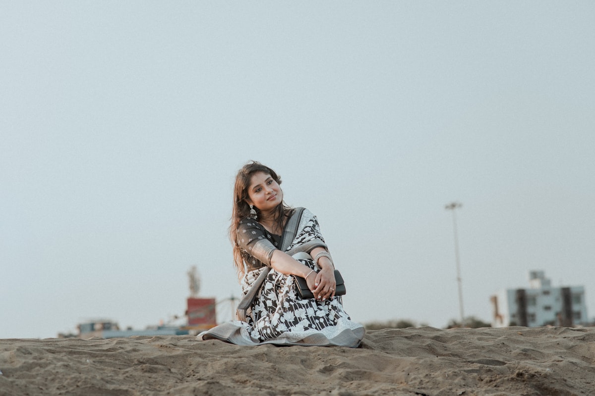 A woman sits on the sand, looking at camera.